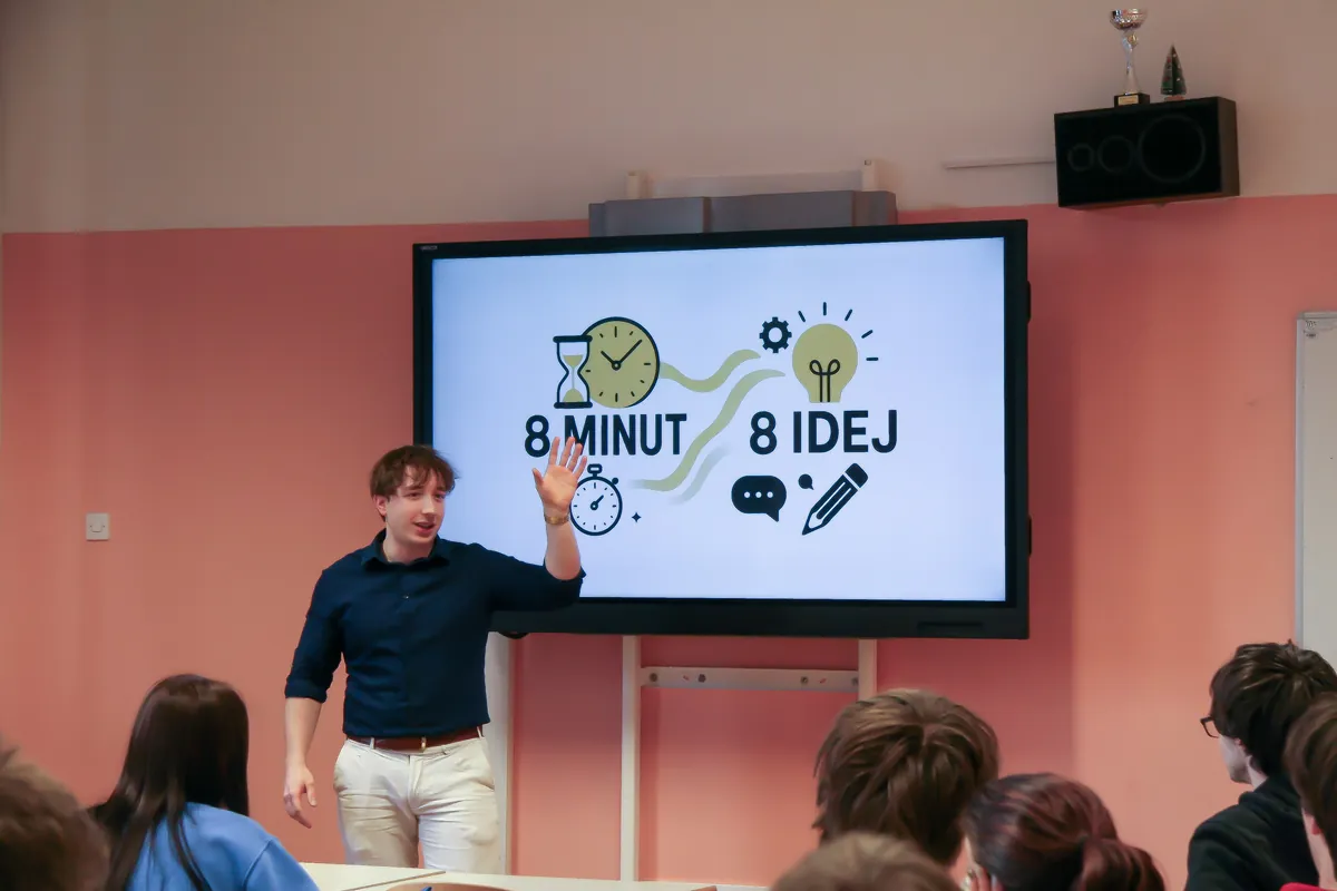 The presenter in front of the classroom screen reading “8 minut 8 idej”, the students seen from behind.