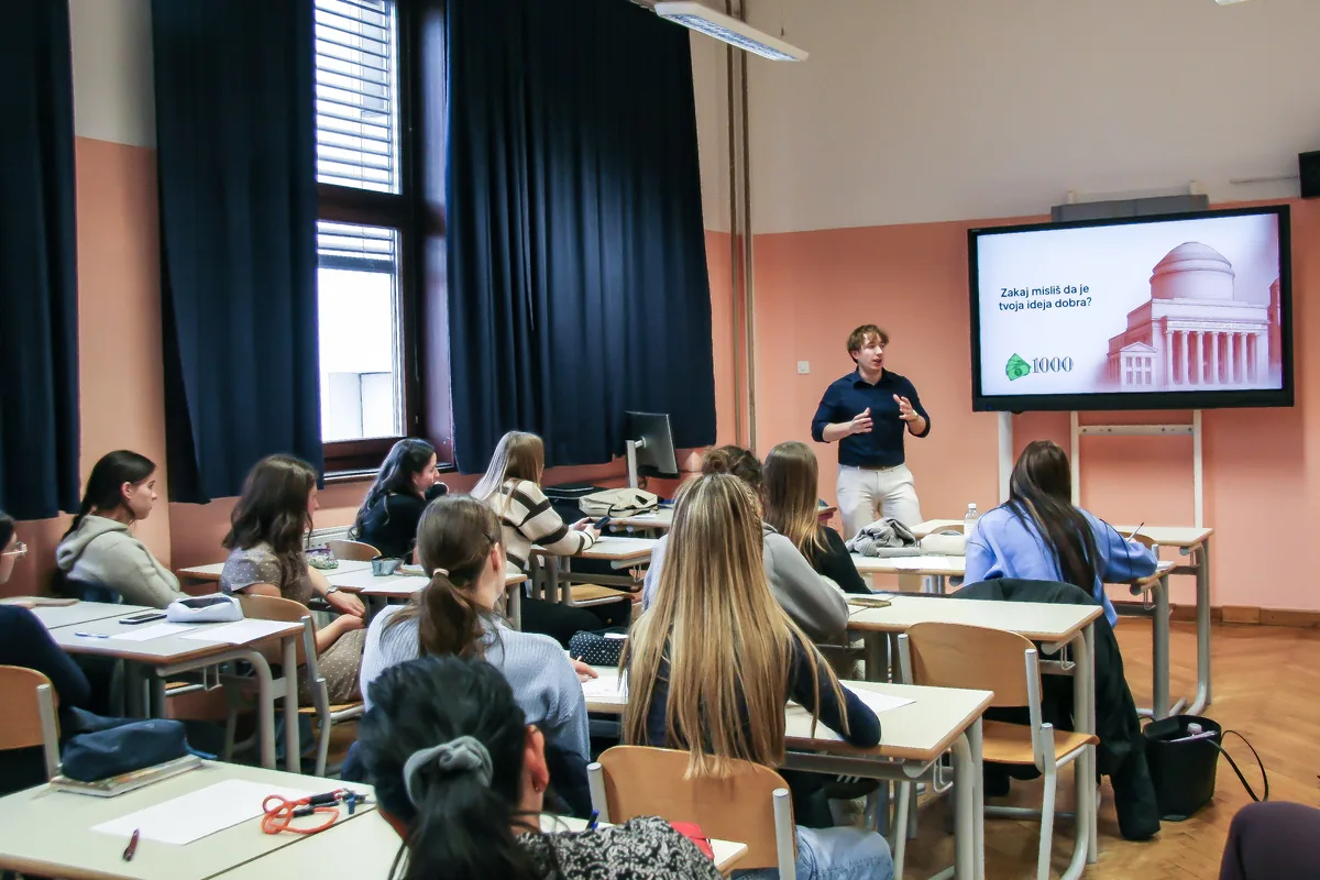 A Global Shapers presenter talking to a class at Gimnazija Bežigrad, the students at their desks with sheets of paper in front of them, the screen behind him asking why you think your idea is good