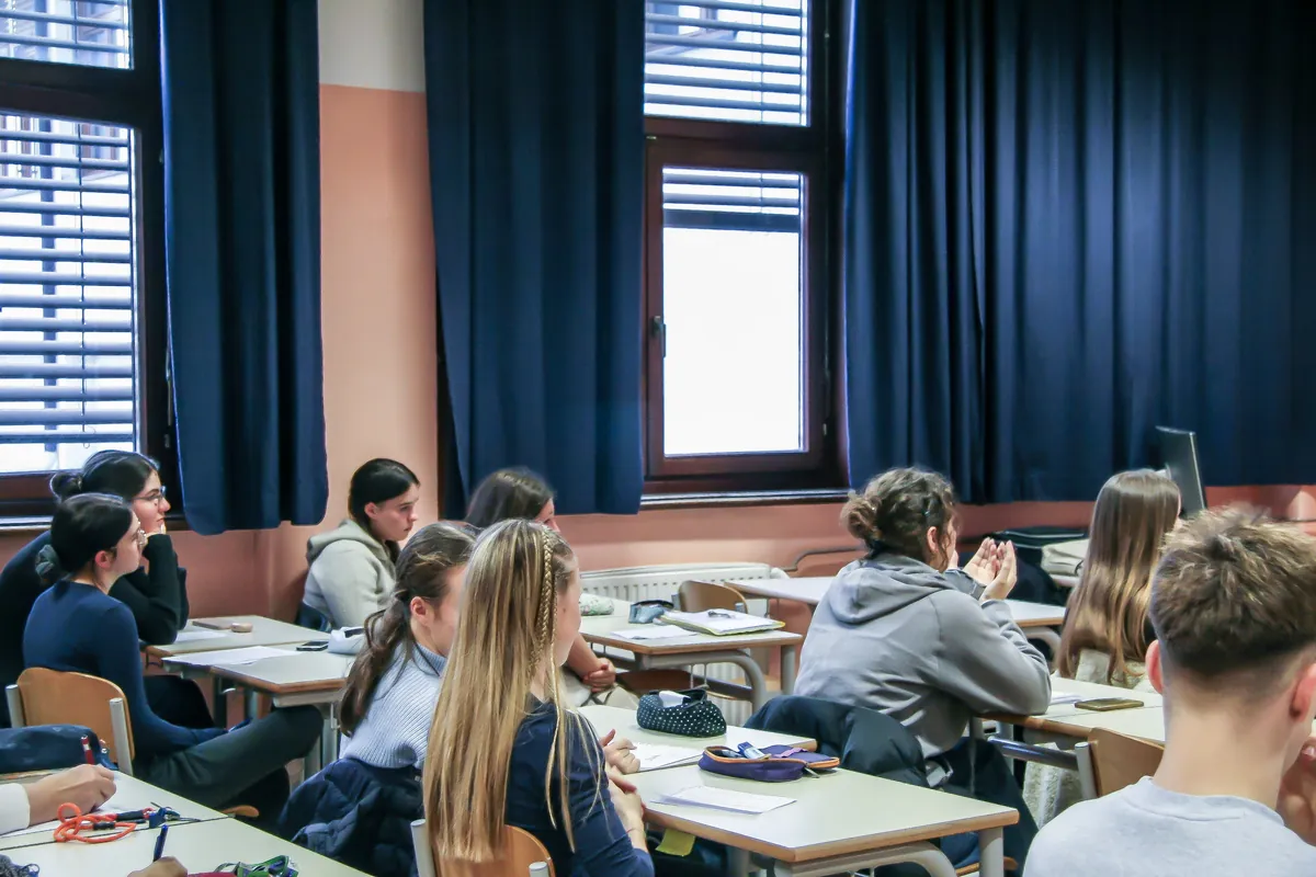 The classroom seen from the back during the visit, students at their desks by the tall curtained windows.