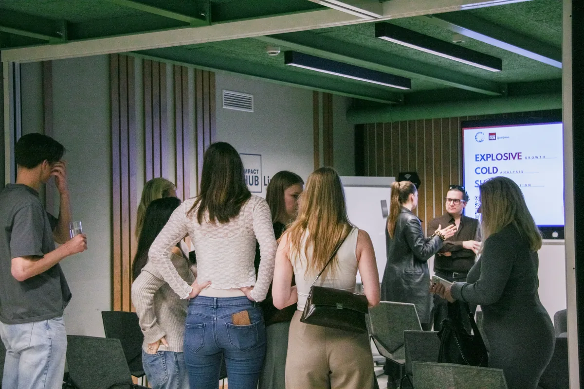 Visitors standing in small groups after the talk at Impact Hub Ljubljana, drinks in hand, the title slide still on the screen behind them.