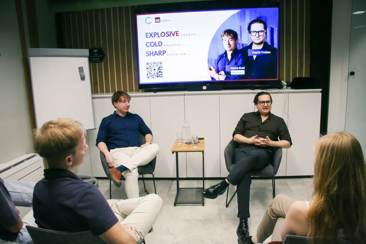 Moderator Marko Grad and guest Patrik Trobec seated opposite each other on the stage at Impact Hub Ljubljana, the talk's title slide behind them and listeners in the front row.