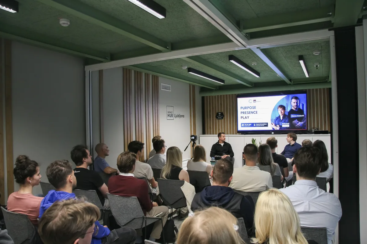 The full event room at Impact Hub Ljubljana seen from the back row, the audience facing the stage where Klemen Selakovič and moderator Marko Grad sit under the “Purpose. Presence. Play.” slide.